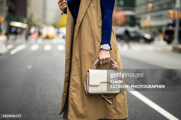 eine frau mit einer smartwatch, die während der arbeitsreichen woche eine tasche auf der straße von manhattan hält - ärmelloser mantel stock-fotos und bilder