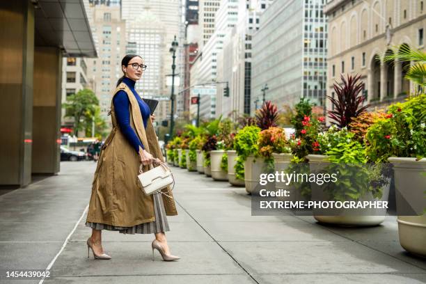 gut gekleidete geschäftsfrau beim verlassen des gebäudes in manhattan nach der arbeit - ärmelloser mantel stock-fotos und bilder