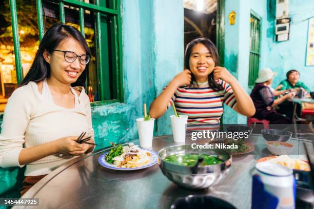 vietnamesische freunde sitzen im straßenrestaurant in hoi an, vietnam - vietnamese street food stock-fotos und bilder