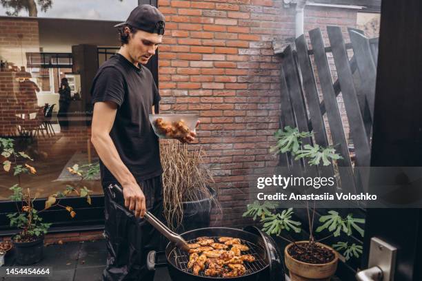 a young man with black hair makes a chicken barbecue in the backyard - hühnchenunterschenkel stock-fotos und bilder