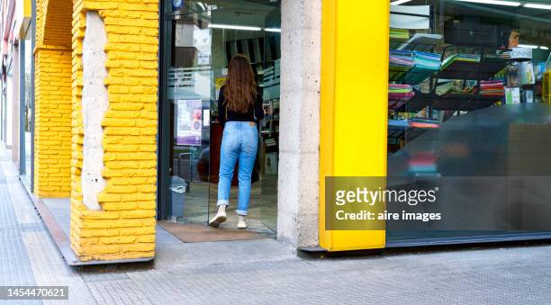 long-haired woman in blue trousers and black sweater entering a print store - entering shop stock pictures, royalty-free photos & images