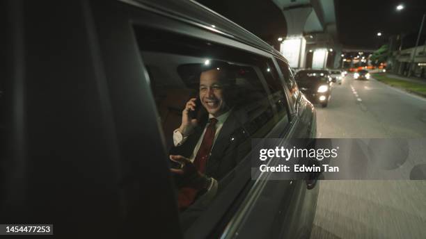 happy asian malay successful businessman talking over phone at back passenger seat at night on the move in city - limo night stock pictures, royalty-free photos & images