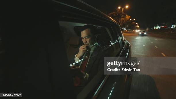 worried asian mature businessman reading text messaging at back seat traveling in city at night - limo stockfoto's en -beelden