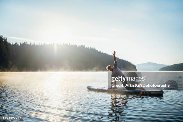 healthy habits improve your wellbeing. - practioners enjoy serenity of paddleboard yoga stockfoto's en -beelden