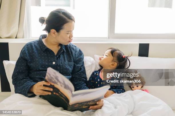 good morning good mood asian mother  telling a story of a picture book for daughter on the bed domestic life - milestone stock-fotos und bilder