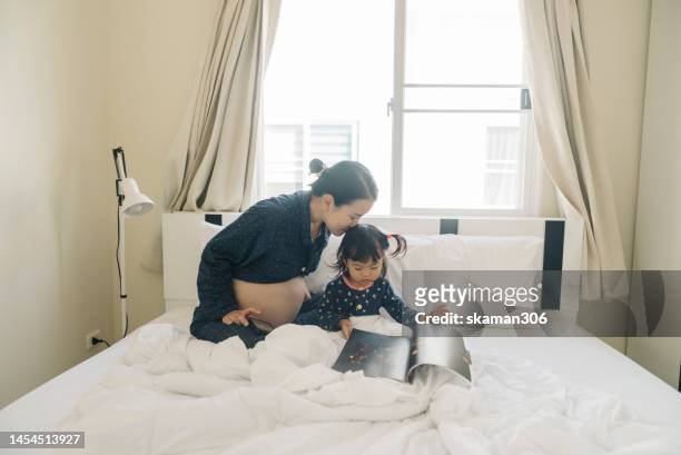 good morning good mood asian mother pregnant second  telling a story of a picture book for daughter on the bed domestic life - tweede kamer stockfoto's en -beelden
