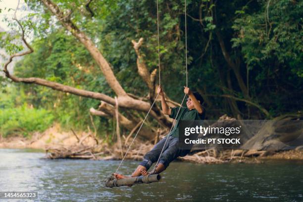 a man in sunglasses swings in the middle of a stream with mountains and forests. - waterfall jump stock pictures, royalty-free photos & images