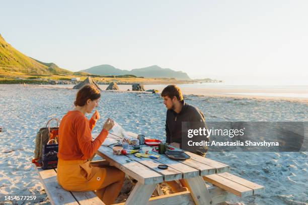 woman and man camping at the scenic beach and having picnic during midnight sun on lofote islands - midnight sun stock pictures, royalty-free photos & images