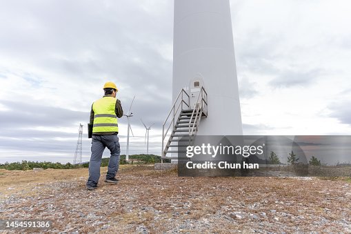 A male worker patrols under the wind turbine on a cloudy day