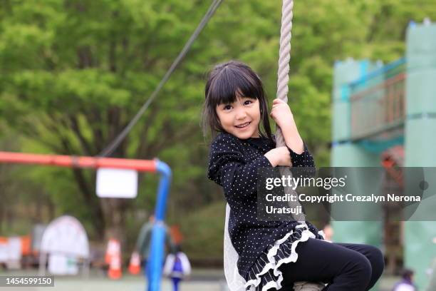 child enjoy hanging on a rope swing at the public park playground. child embracing,holding rope portrait - レギンス　 ストックフォトと画像