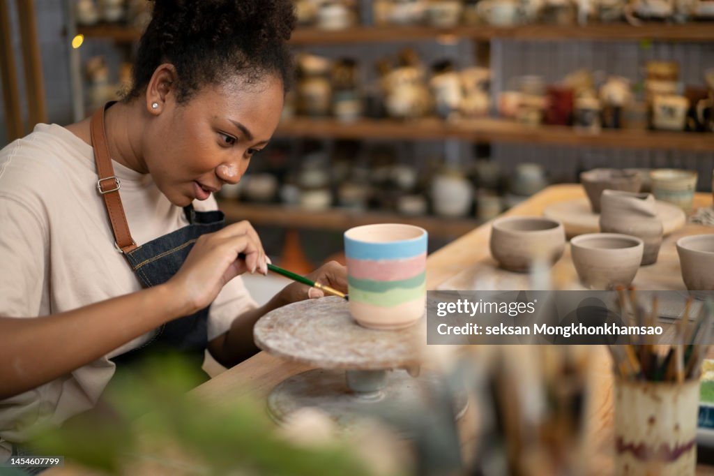Woman painting a cup in her small crafts workshop