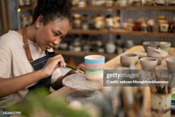 woman painting a cup in her small crafts workshop - painting pottery stock pictures, royalty-free photos & images