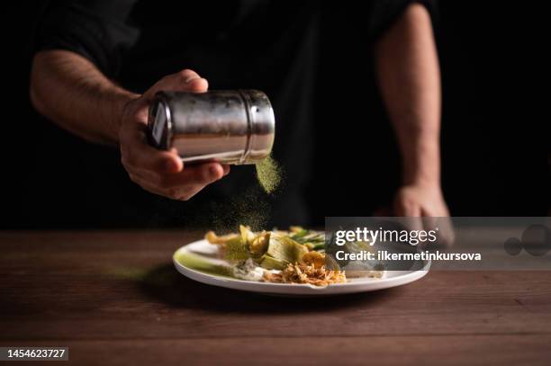 a male chef sprinkling seasonings on a plate of artichoke - kryddning bildbanksfoton och bilder