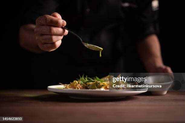 a male chef pouring sauce on on a plate of artichoke - cooked turkey white plate stock pictures, royalty-free photos & images