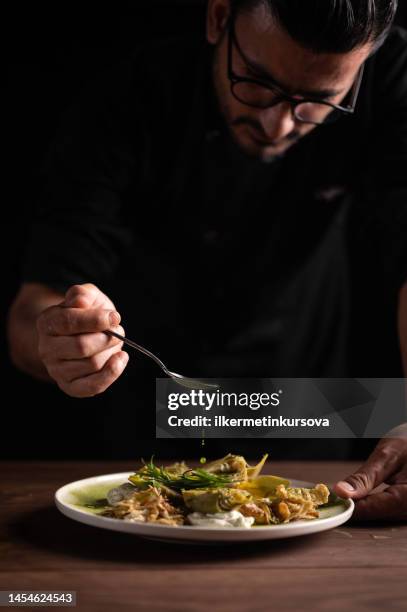 a male chef pouring sauce on on a plate of artichoke - serving dish stock pictures, royalty-free photos & images