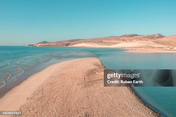 a young woman in a red swimsuit walking on a sandbar on fuerteventura's coast in the atlantic ocean - canary islands 個照片及圖片檔