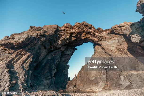 young traveler looking at the ocean under a volcanic arch at sunrise - lava rock stock pictures, royalty-free photos & images