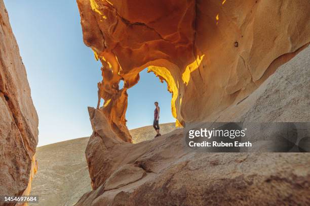 young woman under a natural rock arch in the fuerteventura desert at sunset - travel fotografías e imágenes de stock
