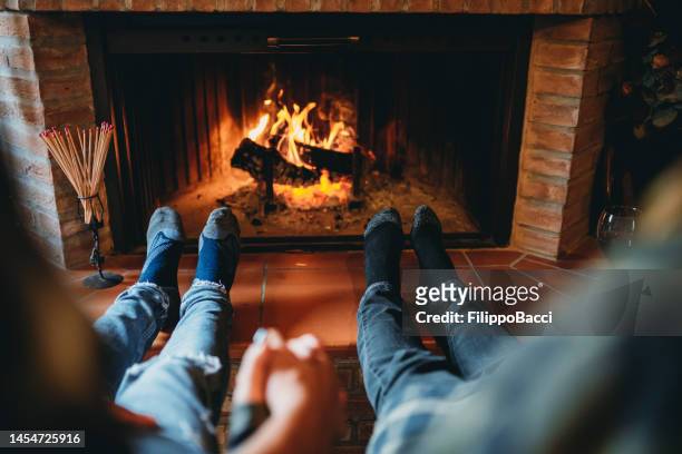 a romantic couple is holding hands in front of the fireplace at home - girlfriend feet stock pictures, royalty-free photos & images