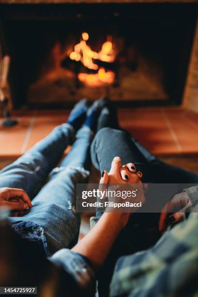 a romantic couple is holding hands in front of the fireplace at home - hot wife stockfoto's en -beelden