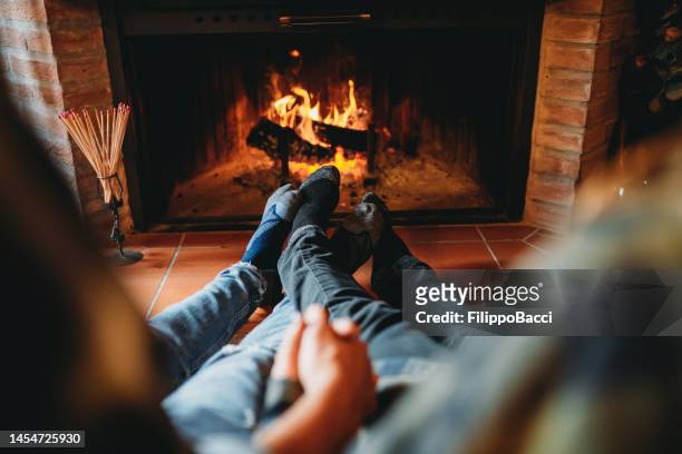 a romantic couple is holding hands in front of the fireplace at home - crush foot stock pictures, royalty-free photos & images