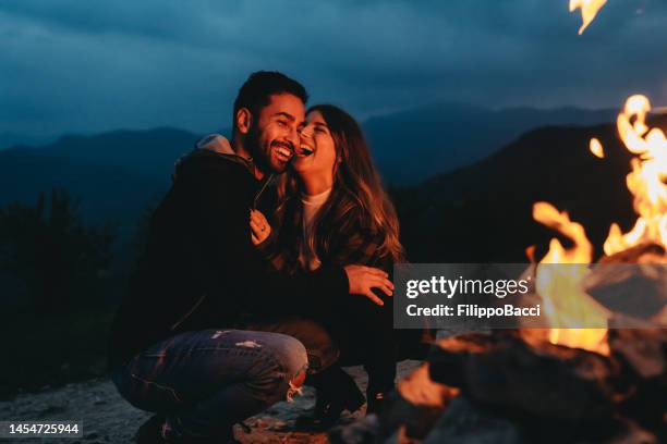 a romantic couple is spending time together near a fireplace outdoor - camping couple stock pictures, royalty-free photos & images