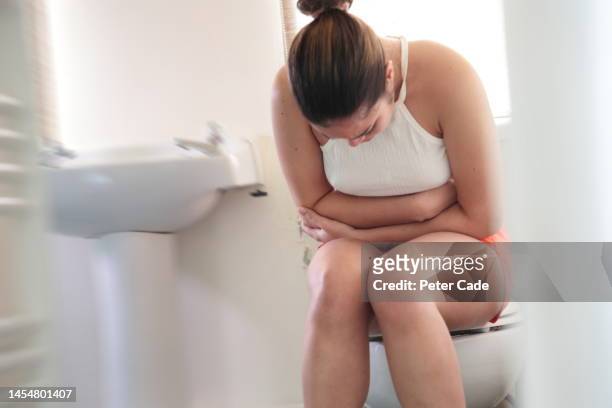 woman sitting on toilet - gastroentérite photos et images de collection