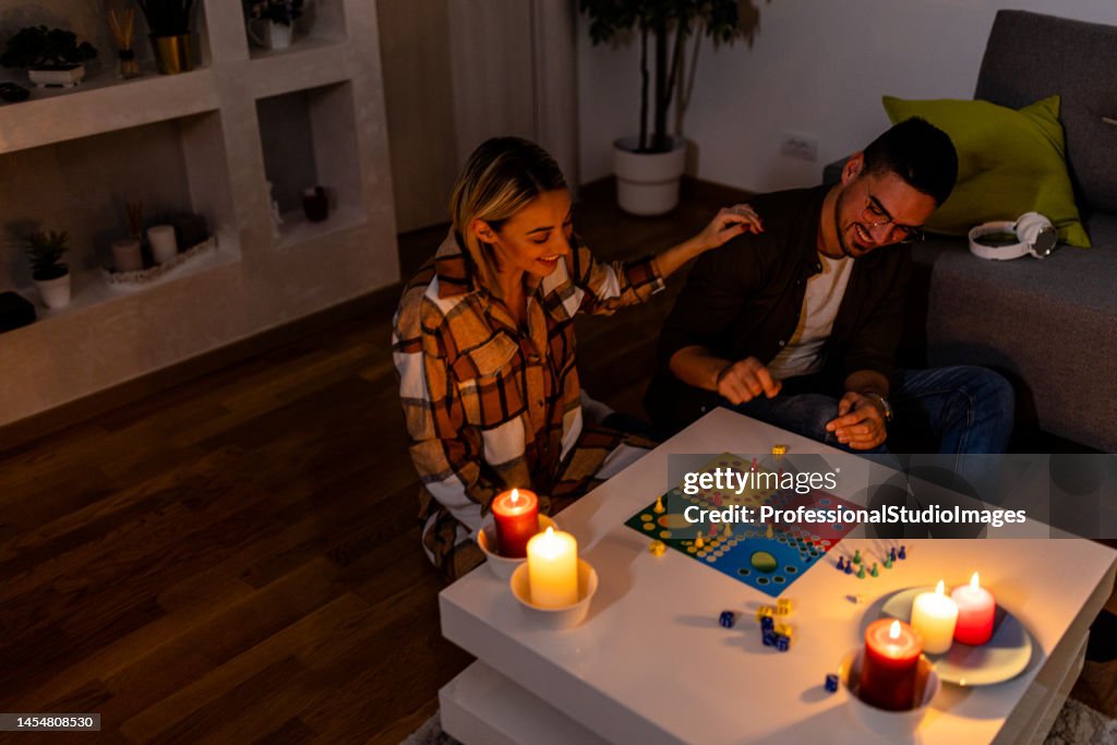 Durante una crisi energetica, un uomo e una donna stanno giocando a un gioco di ludo al buio con candele accese.