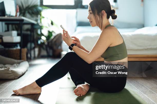young asian woman using fitness app on smartphone to monitor training progress after exercising at home - open workouts stockfoto's en -beelden