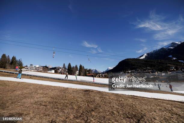 Skiers ride a ski lift alongside a slope covered in artificial snow, while grass covers the rest of the hill on either side on January 07, 2023 in...