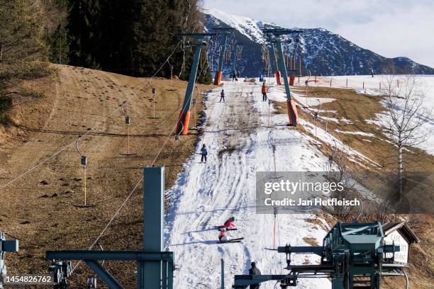 Skiers ride a ski lift on a track covered in artificial snow, while grass covers the rest of the hill on either side on January 07, 2023 in Seefeld,...