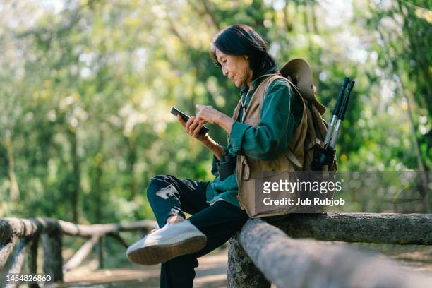 senior asian woman traveling alone in the jungle adventure use your phone happily - answering stock-fotos und bilder