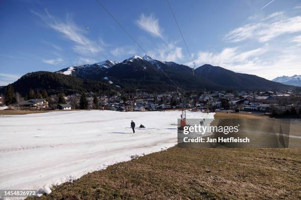 Skiers ride a ski lift alongside a slope covered in artificial snow, while grass covers the rest of the hill on either side on January 07, 2023 in...