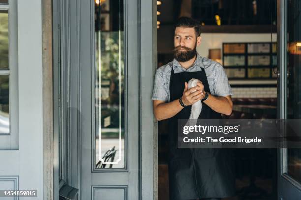 contemplative male waiter standing at doorway of restaurant - barman fotografías e imágenes de stock