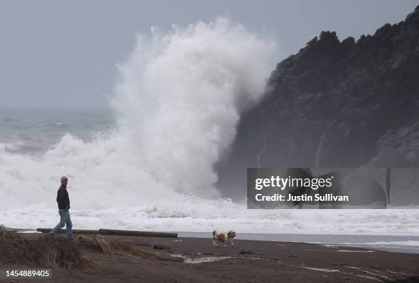 Man walks his dog on the beach as a large wave crashes into shore at Rodeo Beach on January 07, 2023 in Sausalito, California. The San Francisco Bay...