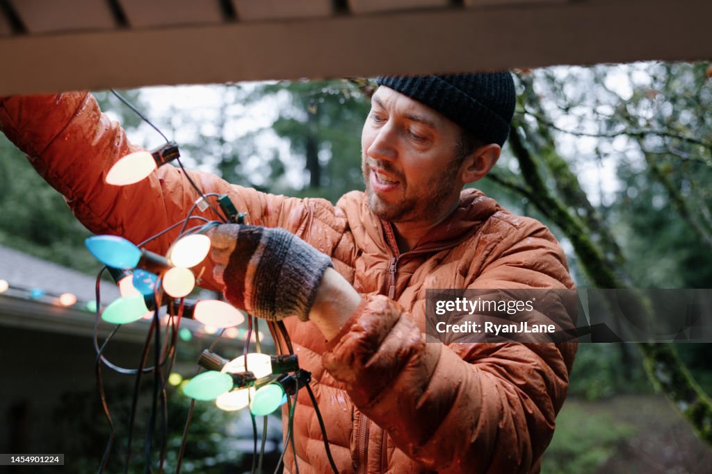 家のクリスマスライトで働く男