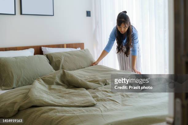 asian woman housewife organizing blankets on the mattress in the bedroom at home. - making bed stockfoto's en -beelden