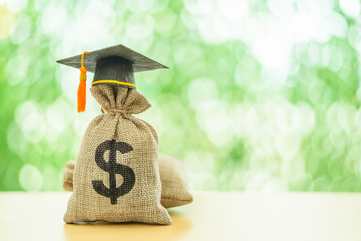 Education or student loan, financial aid and scholarship concept : Mortarboard or graduation cap on top of a US dollar cash bag. Depicting financial assistance for a student