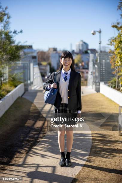 公共の公園に立つ幸せな女子高生の全長のポートレート - 学生服 ストックフォトと画像