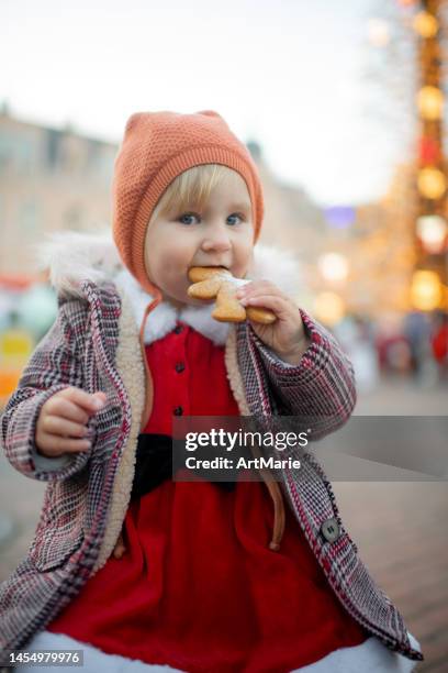 cute little girl eating a gingerbread cookie at a christmas market - winter baby stockfoto's en -beelden