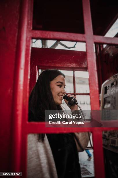 young woman making a call from a red phone booth - telefonzelle stock-fotos und bilder
