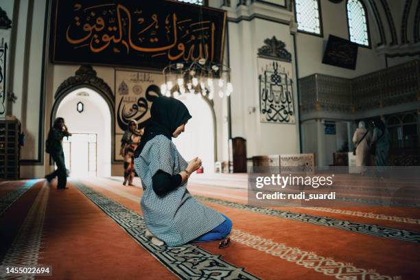 seitenansicht einer frau, die betet, während sie in der moschee kniet - allah stock-fotos und bilder