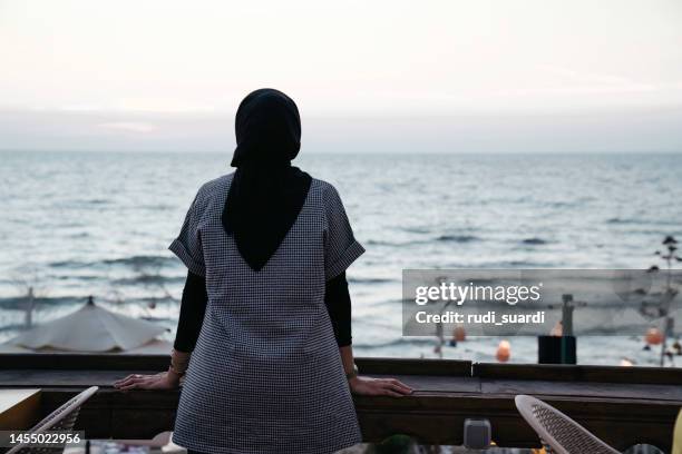 muslim woman looking the beach from the deck - hijab woman from behind stock pictures, royalty-free photos & images