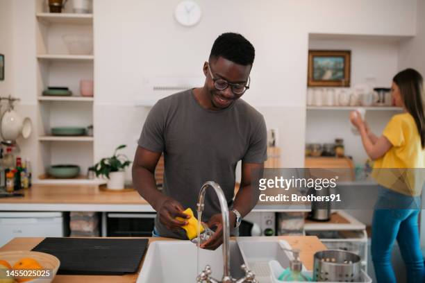 multirassische mitbewohner erledigen hausarbeiten in der küche zu hause - couples showering stock-fotos und bilder