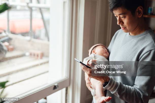 asian father using smart phone while holding his baby - balancearse fotografías e imágenes de stock