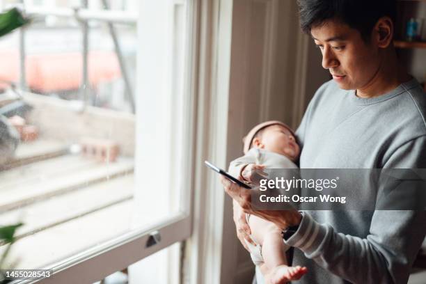 asian father using smart phone while holding his baby - single father 個照片及圖片檔