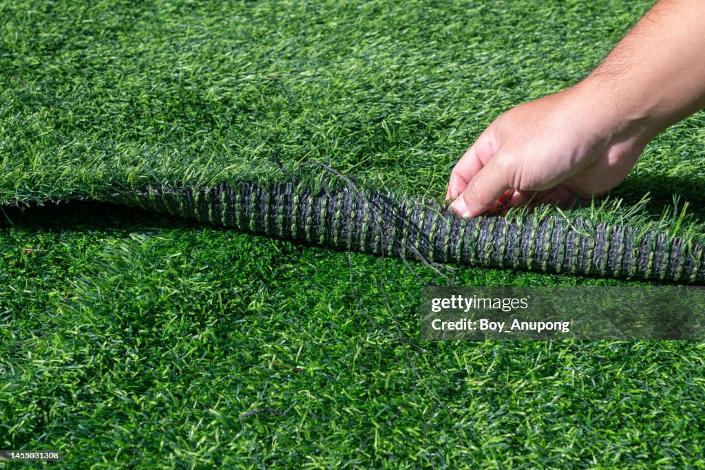 Someone hand pulling an artificial turf before replacement. Artificial turf is used for covering sport arena or garden.