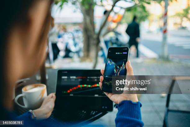 business woman hand using smart phone with cafe shop. stock market charts on phone and laptop  screen. checking financial market. - cryptocurrency trading stock pictures, royalty-free photos & images