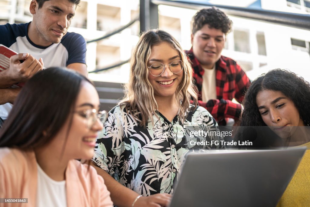 Mujer joven mostrando algo en la computadora portátil a sus amigos en las escaleras de la universidad