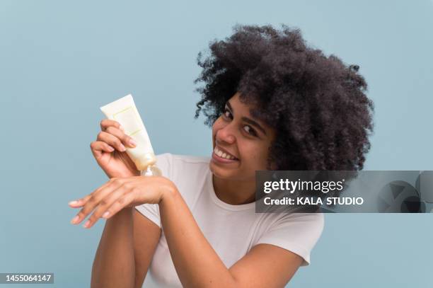 smiling afro brunette girl applying moisturizing cream on her hand looking at camera isolated. - bothies stock pictures, royalty-free photos & images